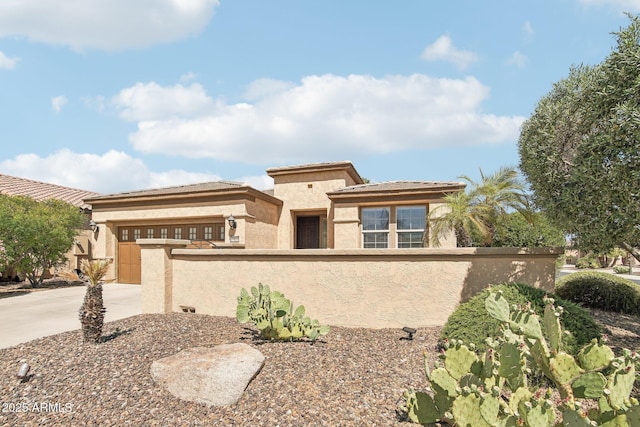 prairie-style home with driveway, stucco siding, a fenced front yard, and an attached garage