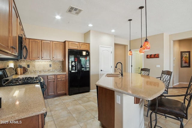 kitchen with a breakfast bar area, a sink, visible vents, black appliances, and tasteful backsplash