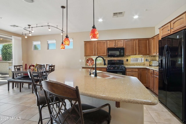 kitchen with light tile patterned flooring, visible vents, a sink, brown cabinets, and black appliances