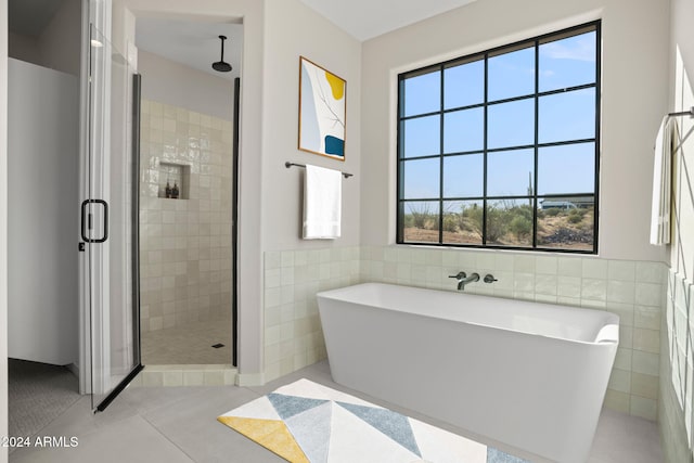 bathroom with tile patterned floors, plenty of natural light, plus walk in shower, and tile walls