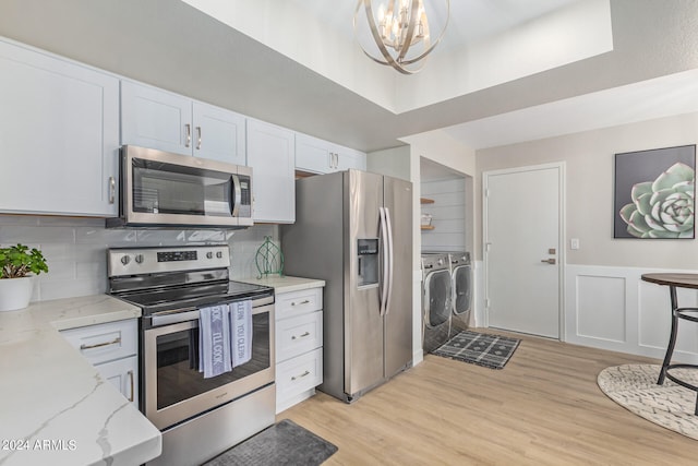 kitchen featuring appliances with stainless steel finishes, light hardwood / wood-style floors, backsplash, white cabinetry, and washing machine and dryer