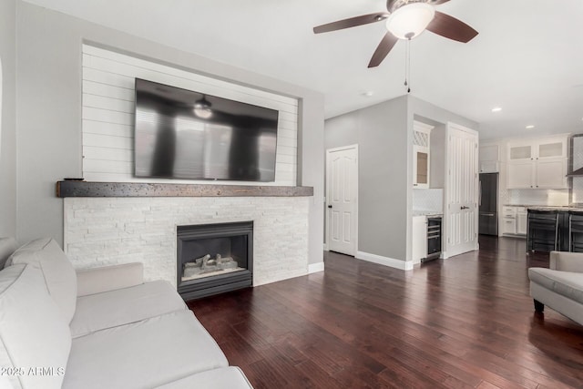 living room with a stone fireplace, beverage cooler, dark hardwood / wood-style floors, and ceiling fan