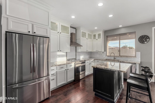 kitchen with wall chimney range hood, sink, appliances with stainless steel finishes, a center island, and light stone counters