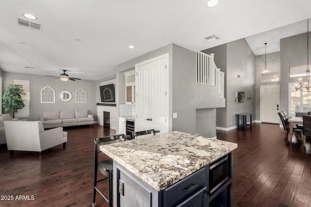 kitchen with dark wood-type flooring, a breakfast bar, hanging light fixtures, a center island, and built in microwave