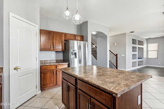 kitchen with stainless steel fridge, light tile patterned floors, a kitchen island, and decorative light fixtures