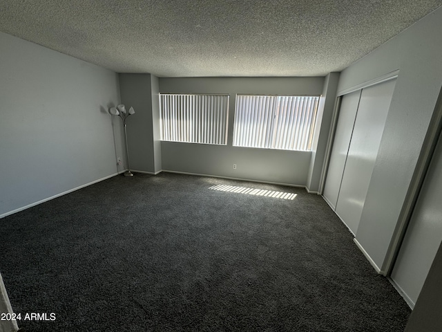 spare room featuring dark carpet and a textured ceiling