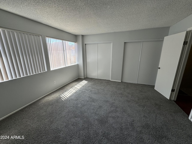 unfurnished bedroom with a textured ceiling, multiple closets, and dark carpet