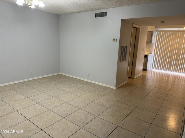 tiled spare room with a chandelier and a textured ceiling