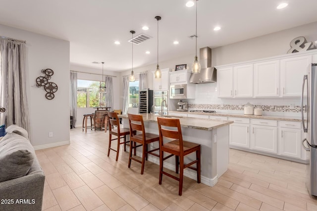 kitchen with wall chimney range hood, backsplash, visible vents, appliances with stainless steel finishes, and white cabinetry