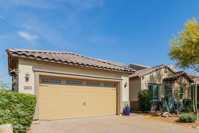 mediterranean / spanish home with an attached garage, decorative driveway, stucco siding, and a tiled roof