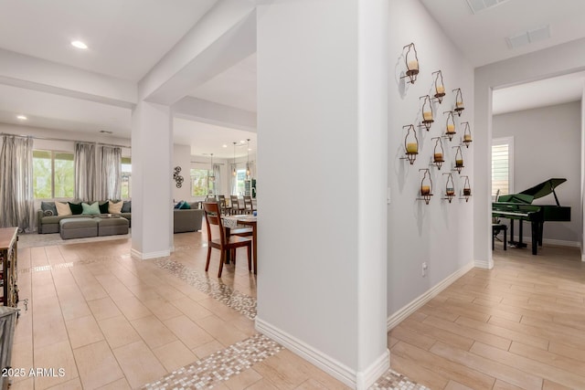 hallway featuring visible vents, light wood finished floors, baseboards, and a wealth of natural light