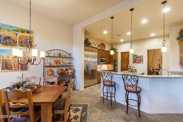 kitchen featuring light stone countertops, appliances with stainless steel finishes, kitchen peninsula, decorative light fixtures, and an inviting chandelier