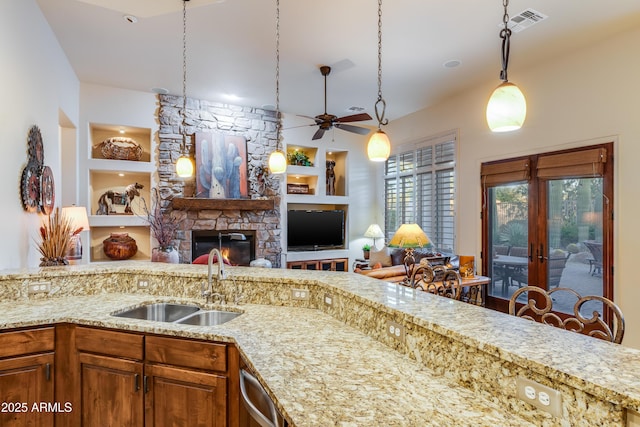 kitchen with built in shelves, ceiling fan, sink, a stone fireplace, and hanging light fixtures