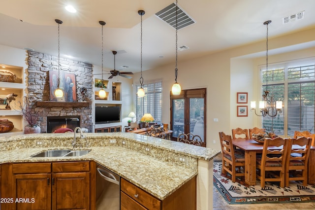 kitchen featuring ceiling fan with notable chandelier, sink, hanging light fixtures, a fireplace, and light stone counters