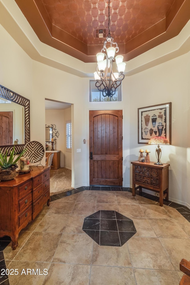 foyer entrance featuring a raised ceiling, a towering ceiling, and a notable chandelier