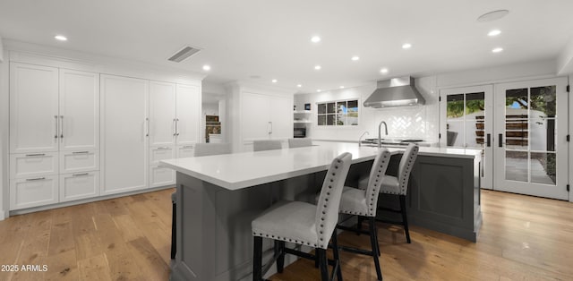 4824 E Hummingbird Ln, Paradise Valley, AZ 85253 - kitchen with wall chimney exhaust hood, light wood-style flooring, white cabinets, a spacious island, and recessed lighting