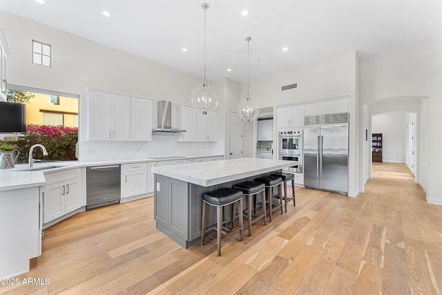 kitchen featuring white cabinetry, stainless steel appliances, a center island, and wall chimney exhaust hood