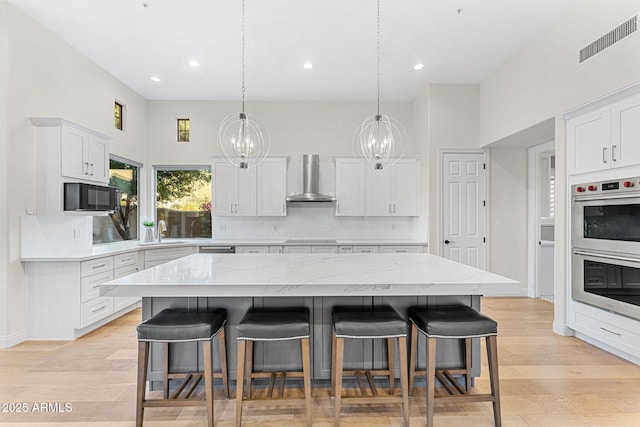 kitchen with a kitchen island, white cabinets, a kitchen bar, black appliances, and wall chimney range hood