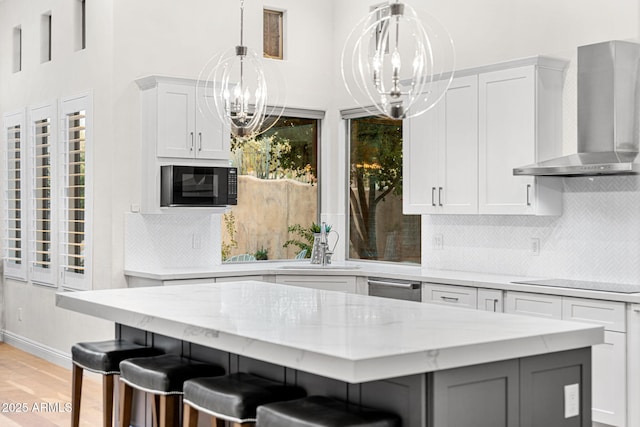 kitchen featuring a breakfast bar, white cabinetry, black microwave, a kitchen island, and wall chimney range hood