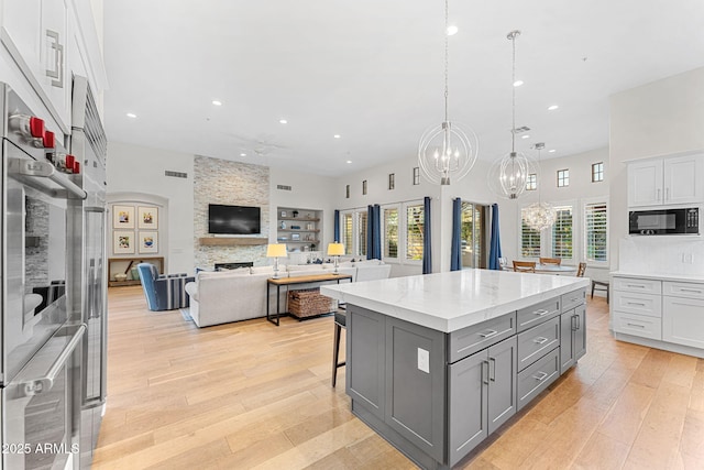 kitchen featuring a kitchen island, a fireplace, white cabinetry, black microwave, and hanging light fixtures