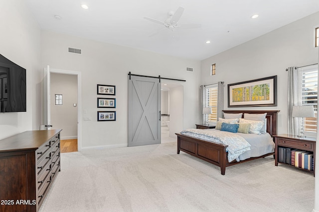 carpeted bedroom with a barn door, ceiling fan, and ensuite bathroom