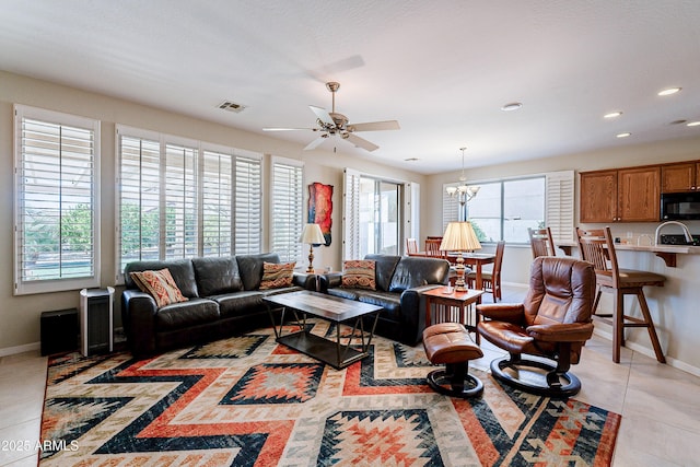 tiled living room with ceiling fan with notable chandelier