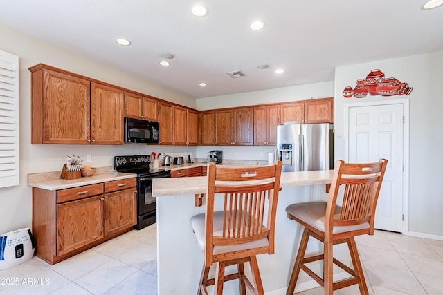 kitchen featuring light tile patterned floors, a center island, a breakfast bar area, and black appliances