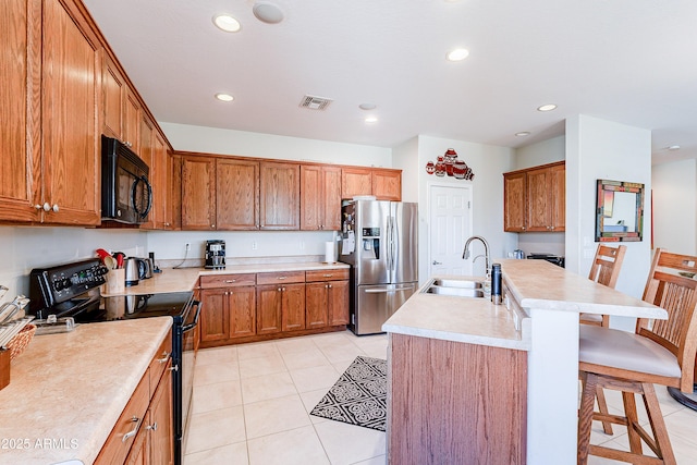 kitchen featuring a kitchen island with sink, black appliances, a kitchen breakfast bar, sink, and light tile patterned floors