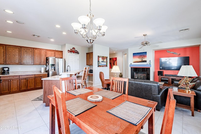 tiled dining area with ceiling fan with notable chandelier, sink, and a fireplace