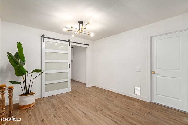 bedroom with a barn door, light hardwood / wood-style flooring, and an inviting chandelier