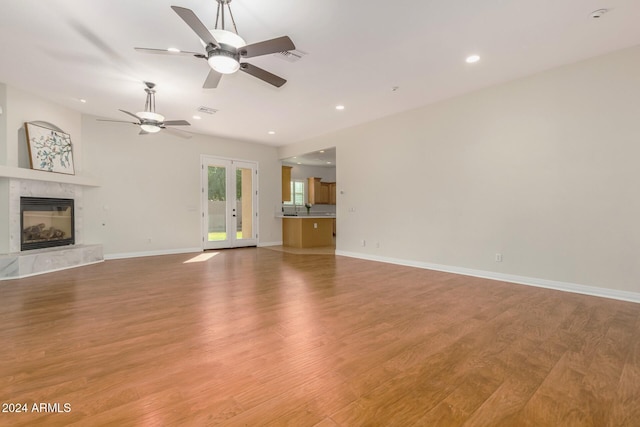 unfurnished living room featuring french doors, ceiling fan, a fireplace, and light wood-type flooring