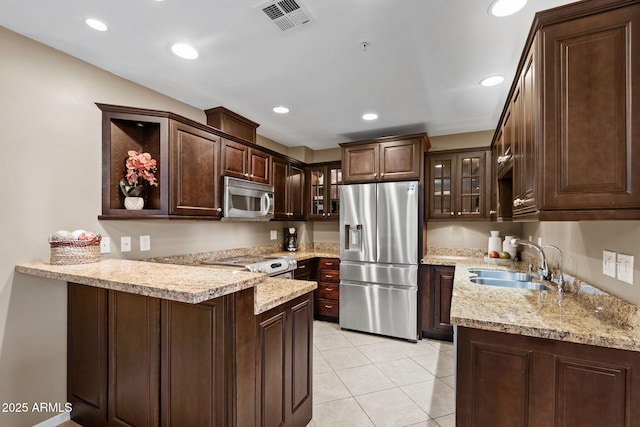 4200 N Miller Rd Unit 408, Scottsdale, AZ 85251 - kitchen featuring appliances with stainless steel finishes, dark brown cabinetry, glass insert cabinets, a peninsula, and light tile patterned flooring