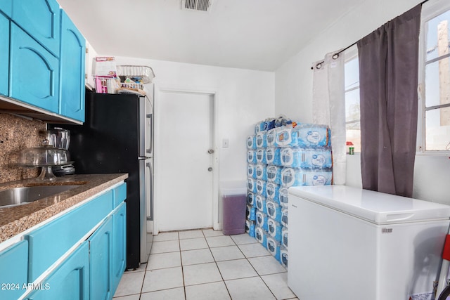 kitchen featuring black refrigerator, backsplash, blue cabinets, light tile patterned floors, and white fridge