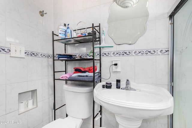 bathroom featuring toilet, tile walls, a shower with shower door, and sink