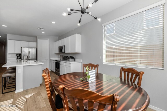 dining area featuring an inviting chandelier, sink, and light hardwood / wood-style flooring