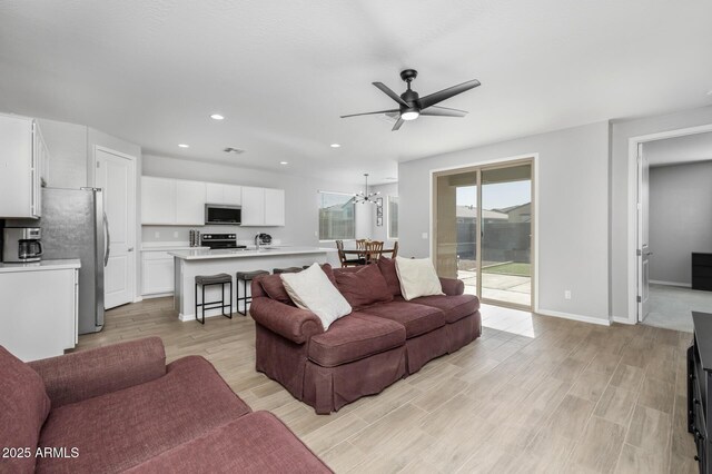 living room with ceiling fan with notable chandelier and light hardwood / wood-style floors