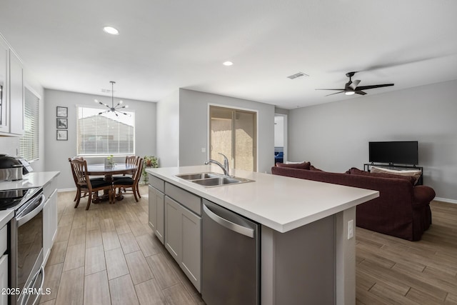 kitchen with a kitchen island with sink, ceiling fan with notable chandelier, hanging light fixtures, sink, and appliances with stainless steel finishes