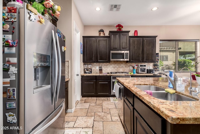 kitchen featuring sink, decorative backsplash, dark brown cabinets, light stone counters, and stainless steel appliances