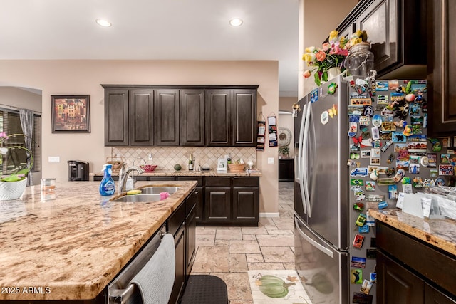 kitchen with backsplash, sink, light stone counters, dark brown cabinetry, and stainless steel appliances