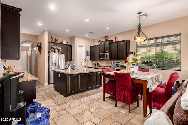 kitchen featuring light stone counters, dark brown cabinetry, stainless steel appliances, pendant lighting, and a center island