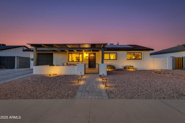 view of front of house with an attached garage, a fenced front yard, solar panels, and stucco siding