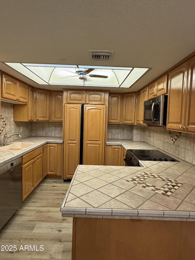 kitchen featuring dishwashing machine, tile countertops, visible vents, a sink, and range