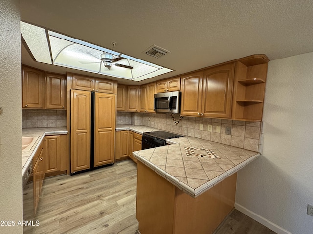 kitchen with electric range, stainless steel microwave, a peninsula, a skylight, and light wood finished floors