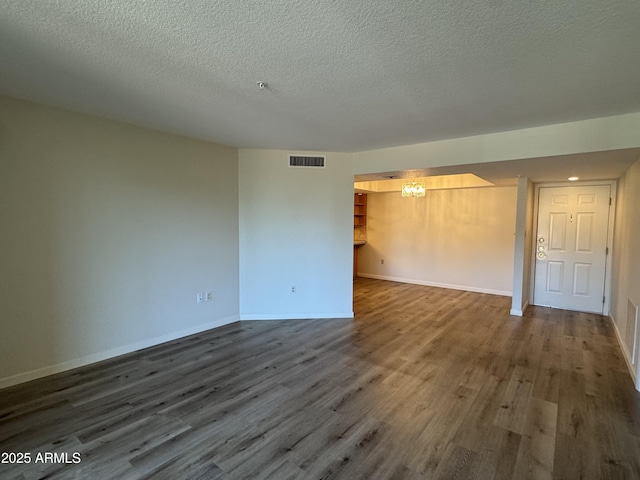 unfurnished room featuring a textured ceiling, wood finished floors, visible vents, and baseboards