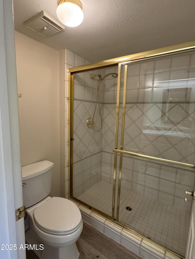 full bathroom with visible vents, a shower stall, toilet, wood finished floors, and a textured ceiling