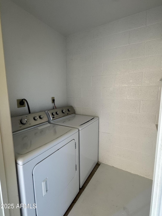 clothes washing area with laundry area, concrete block wall, and washing machine and clothes dryer