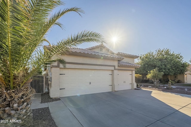 view of side of home featuring driveway, an attached garage, a tiled roof, and stucco siding