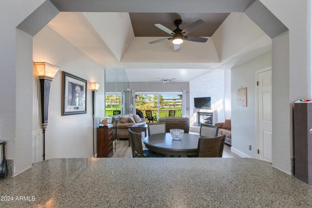 dining area with a glass covered fireplace, a raised ceiling, and ceiling fan