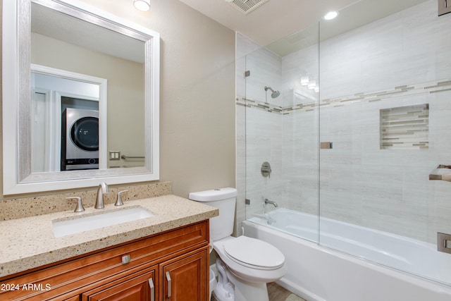 bathroom with visible vents, toilet, stacked washing maching and dryer, combined bath / shower with glass door, and vanity