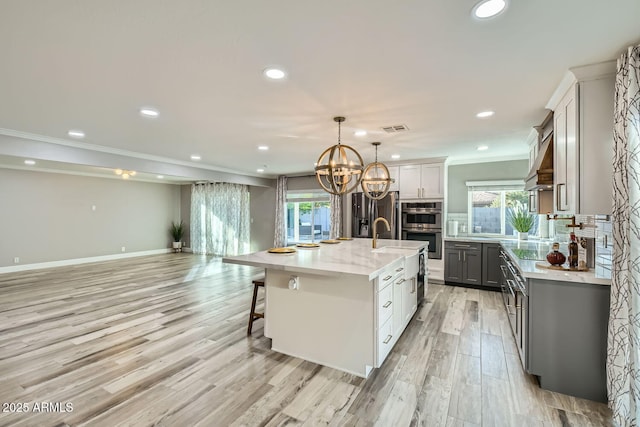 kitchen with light hardwood / wood-style flooring, pendant lighting, a kitchen island with sink, gray cabinetry, and appliances with stainless steel finishes